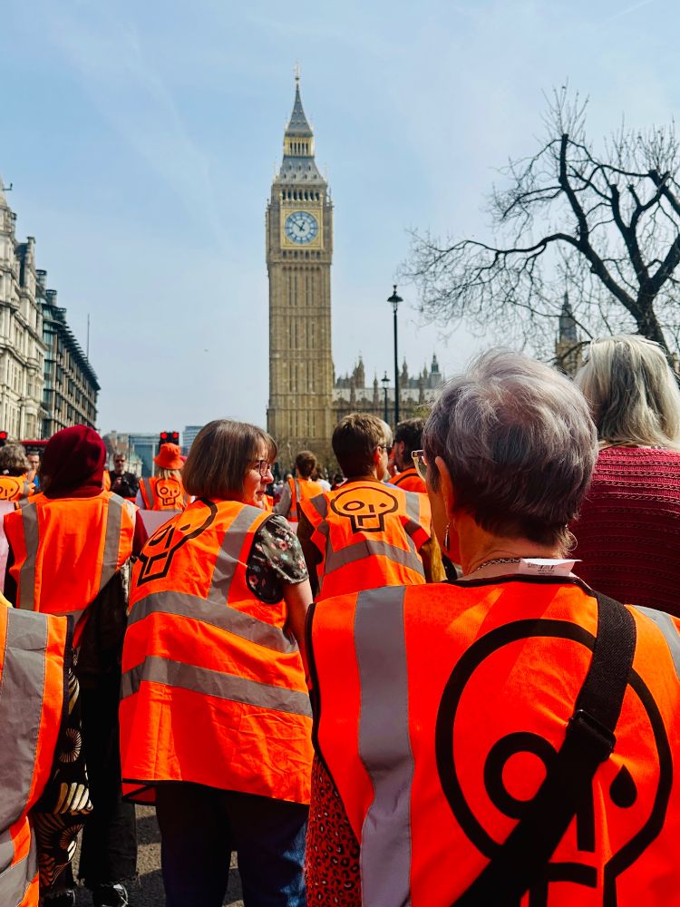 Protestors wearing bright orange high vis jackets with the just stop oil logo march past Big Ben 