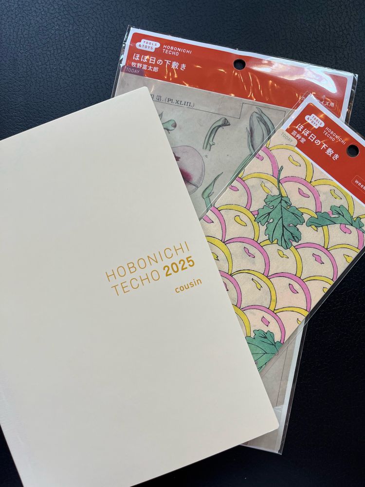 Photo of the front cover of the Hobonichi Techo 2025 planner, with two pencil boards tucked behind the right corner.
