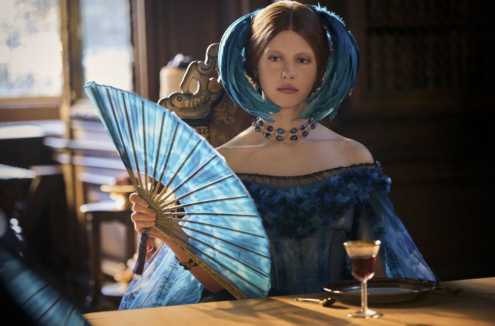 Photo of Mia Goth, dressed in a blue feathered headress and holding a blue fan, playing as Elizabeth Lavenza, Victor Frankenstein's fiancée, in Guillermo del Toro's new adaptation.