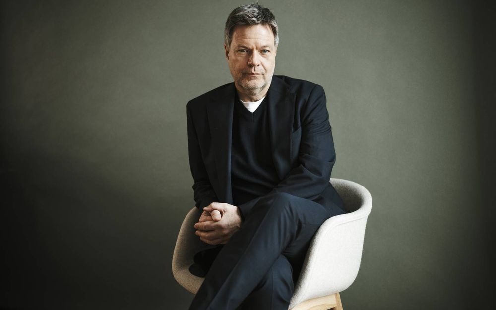 Robert Habeck mit einem angenehmen, modernen Politikerportrait.
Er trägt ein V-neck-Strickstück über einem weißen Shirt mit einem angenehm schlank geschnittenen, mattschwarzen modernen Anzug. Es ist ein interessant subtiles Potpourri aus Stilen, die insgesamt aber einen schönen haptischen Kontrast und Anekdote auf einen white-collar schaffen - jedoch ohne steif zu wirken. Ein wenig wie ein Marketingmensch, aber bequemer. Ein angenehmes Politikerbild, was auch zum bestimmten und informierten Redestil passt. 
Der Hintergrund ist ein warmes Beige mit leichter Textur, als Spotlight ausgeleuchtet. 
Habeck selbst sitzt in einem Schalensessel, der ein wenig an schwedisches Design erinnert, schief, mit überschlagenen Beinen.
Für einen Mann eine recht sanfte, junge und zurückhaltende Pose, die aber ihm eine gewisse Grundfeste und Überlegtheit ausstrahlen.

Ein schöne, modernes Politikerportrait eines Menschen, den man leider wie so viel Intelligenz aus diesem Land gemobt hat...