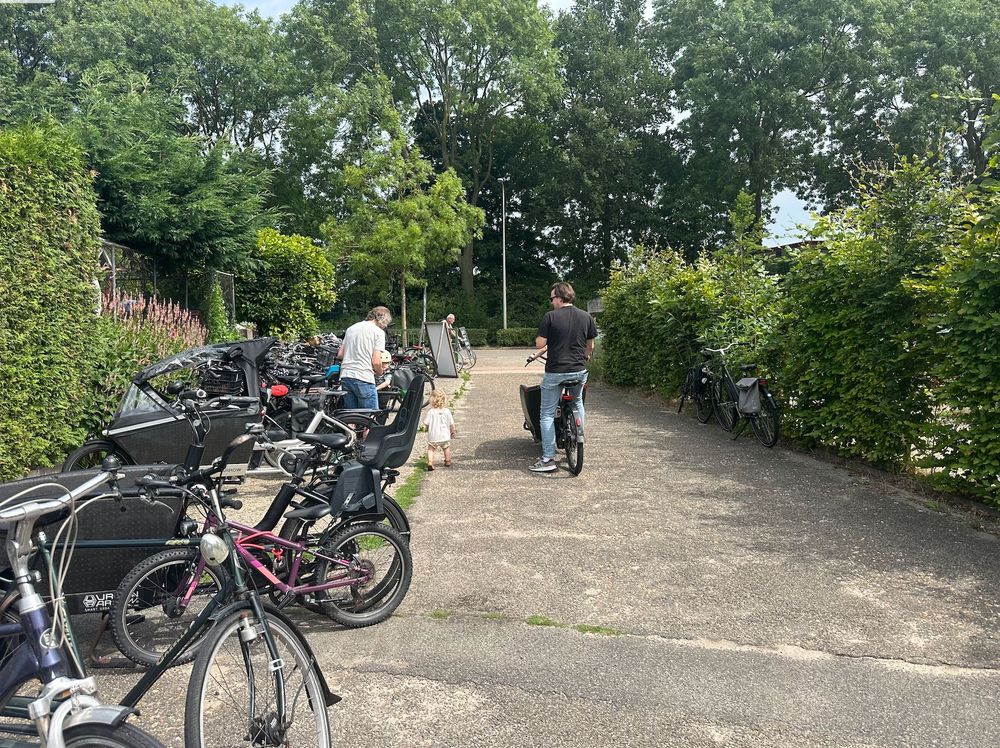 Parents loading their small children into cargo bikes in the parking lot. / Ouders laden hun kleine kinderen in de bakfietsen op de parkeerplaats.
