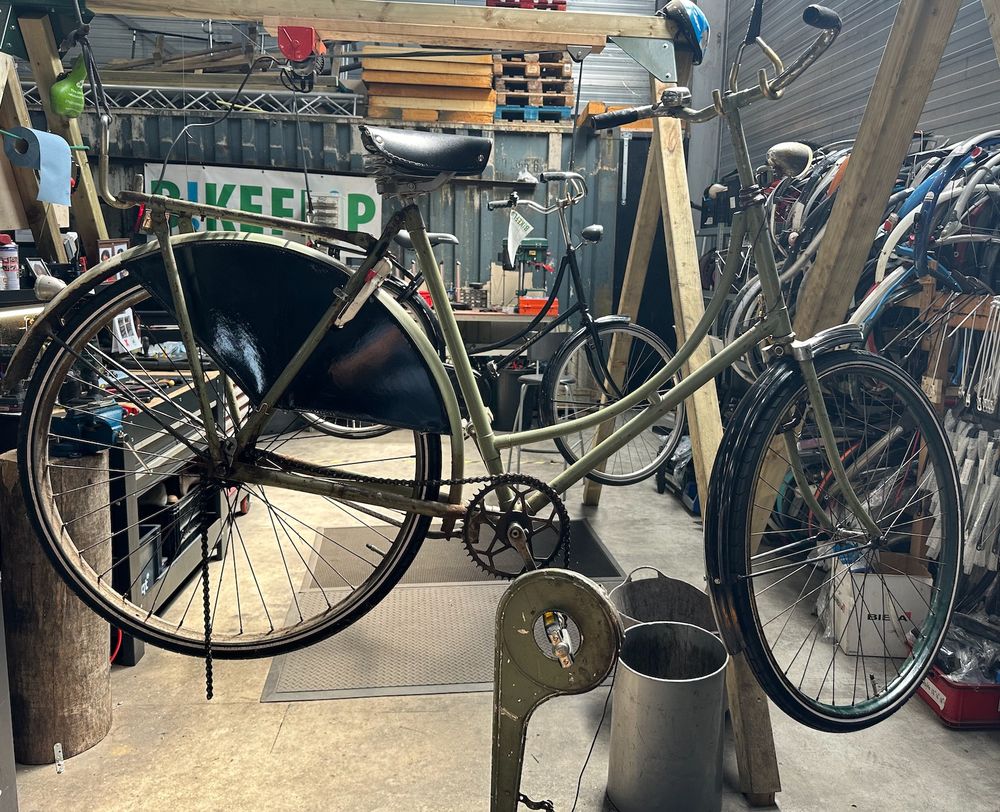 The upright bike on a hanging on a repair lift in front of the BikeFlip sign. One of my co-workers said these were the sort of bikes taken by the Germans in WWII and melted down for munitions, infuriating the Dutch! https://www.dutchnews.nl/2009/04/german_wants_to_pay_for_stolen/