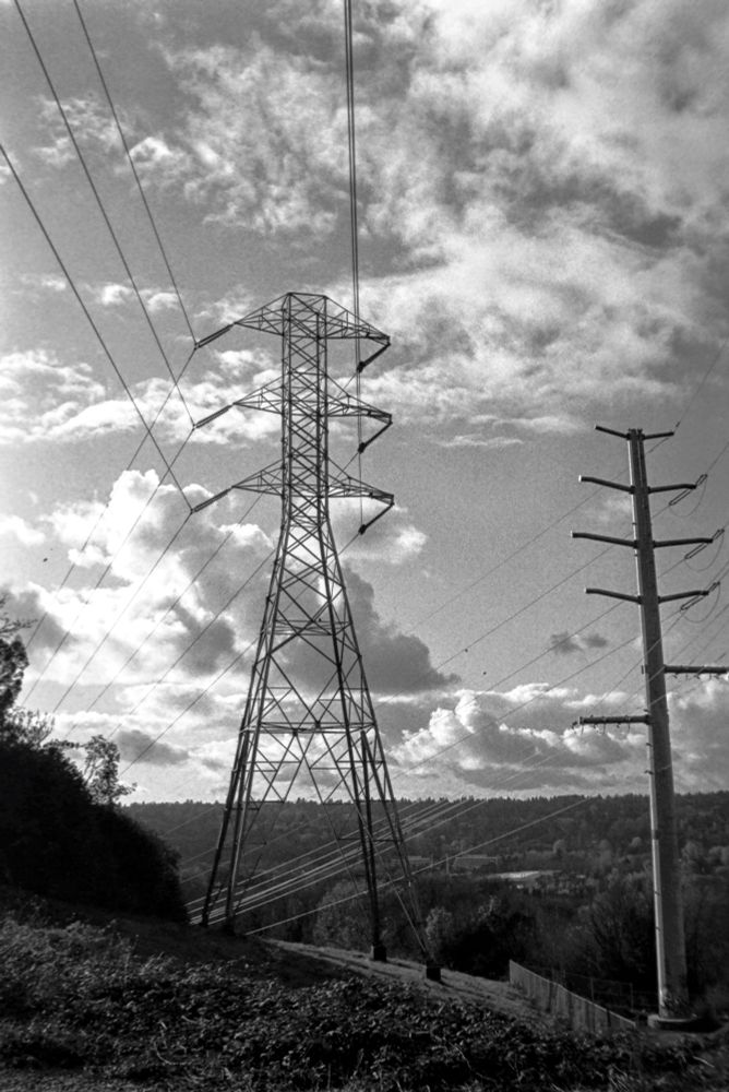 Two power line towers with a valley behind. Happy clouds above