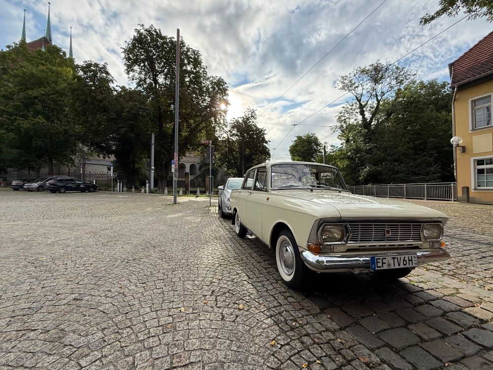 Verzerrte Aufnahme des Autos von vorn. Schön anzusehen die verchromte Frontpartie. Im Hintergrund einige Bäume und drei Spitzen einer Kirche.
