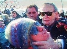 Man being grabbed by his face in a non-friendly manner, by an older gentleman wearing Ray-Ban sunglasses 