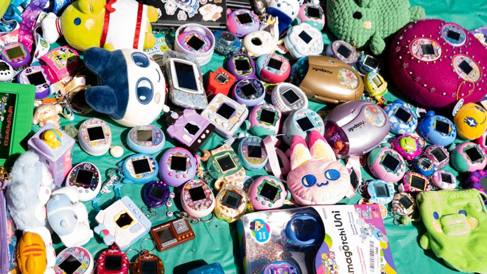 A photo of a bunch of Tamagotchi from varying generations in a pile because the SF Bay Area Tamagotchi Club got together today for our second annual summer picnic 