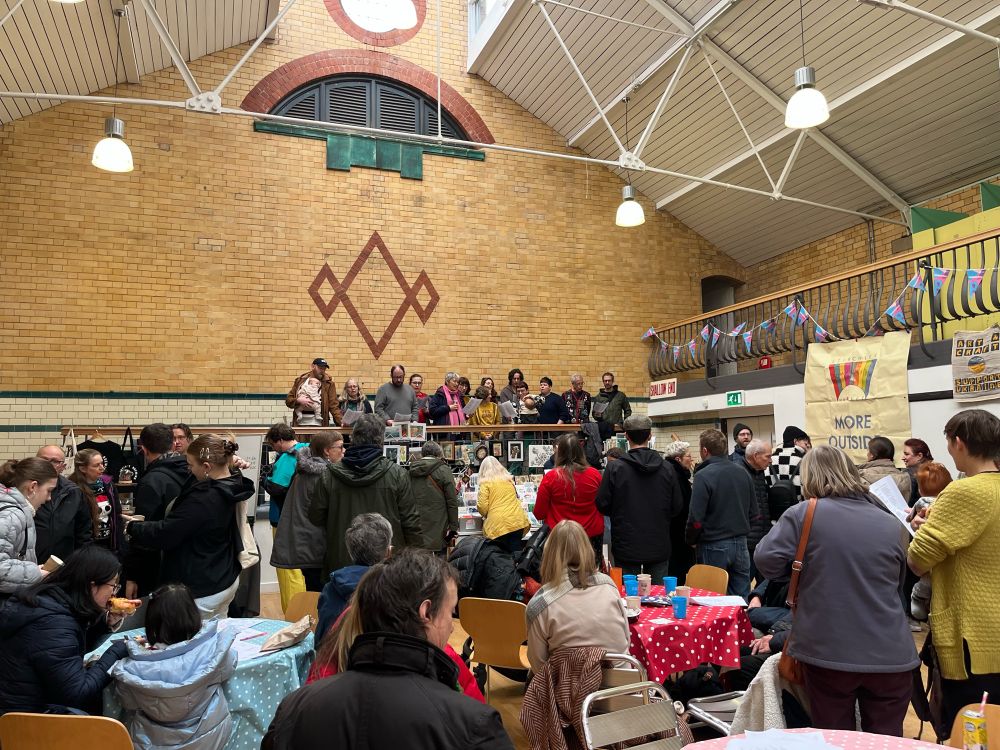 Crowd watching singing group, in a refurbished swimming baths now a community hall 