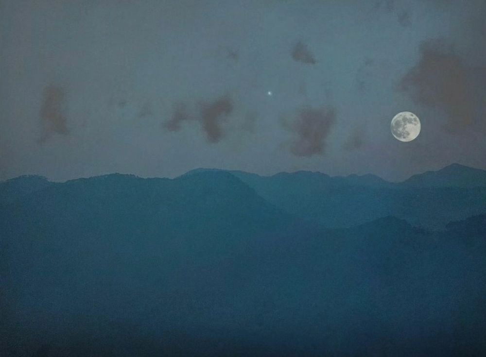 35mm colour photograph. Landscape of the Shivalik range - blue gradient mountains, with a bright full moon and a single star visible in the sky. Wispy plum coloured clouds offer some contrast. 