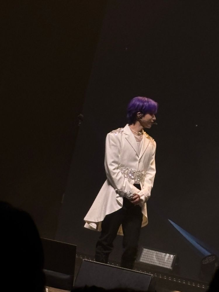 A member of ONEUS on stage wearing a white sparkly coat. 
