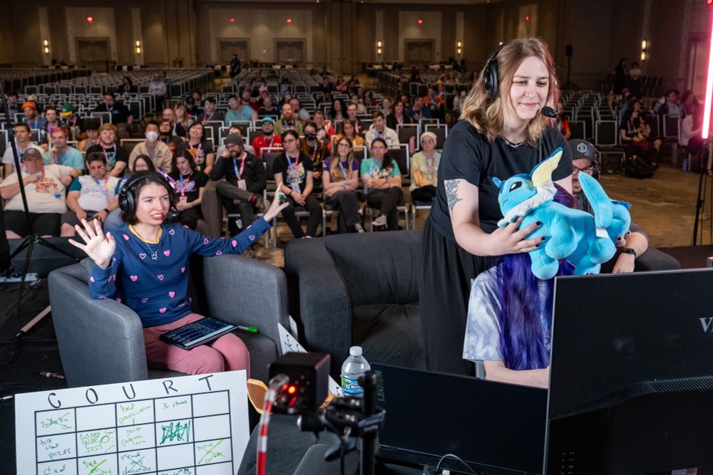 A photo of Izzy covering Greta’s eyes using a Vaporeon plushie, a makeshift blindfold for the blindfolded teacup puzzle incentive. Court is watching intently, and the crowd is seen behind us.