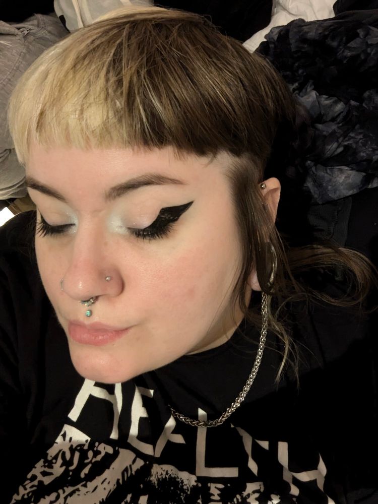 Reva is lay down with his eyes closed. He is wearing thick winged eyeliner.