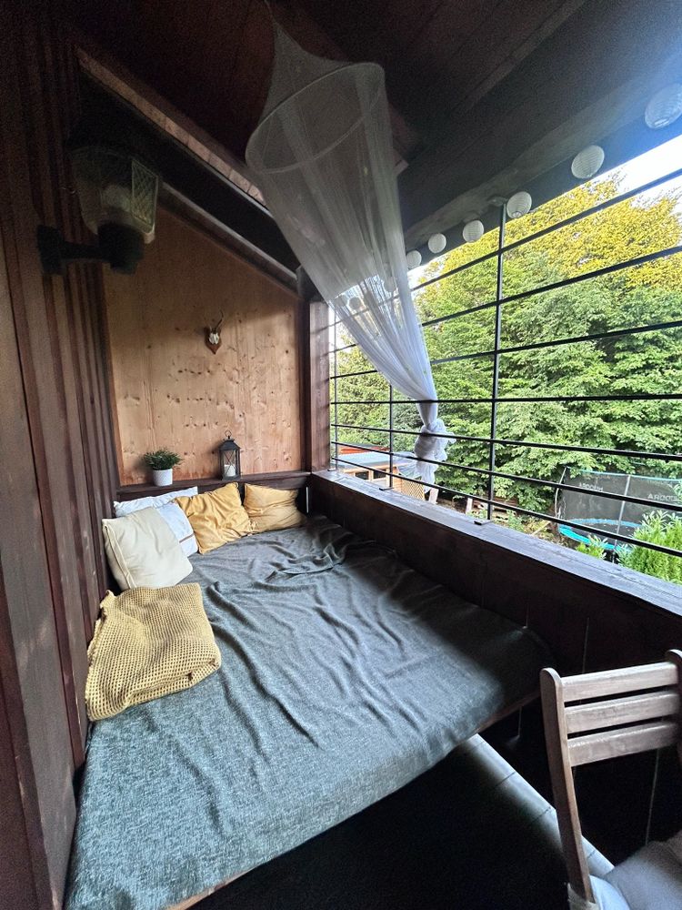 Eine Liegeecke auf einem überdachten Balkon mit Kissen und Moskitonetz.