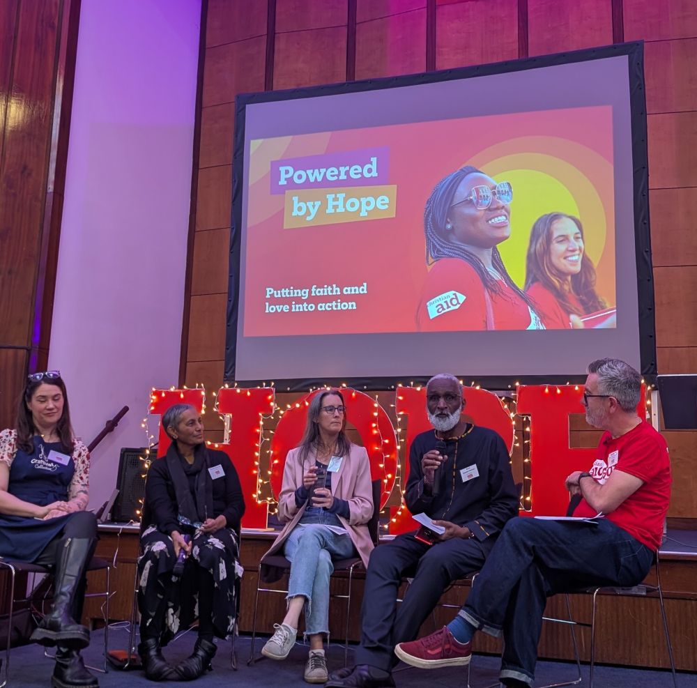 Opening panel of speakers with a screen reading Powered by Hope behind 
