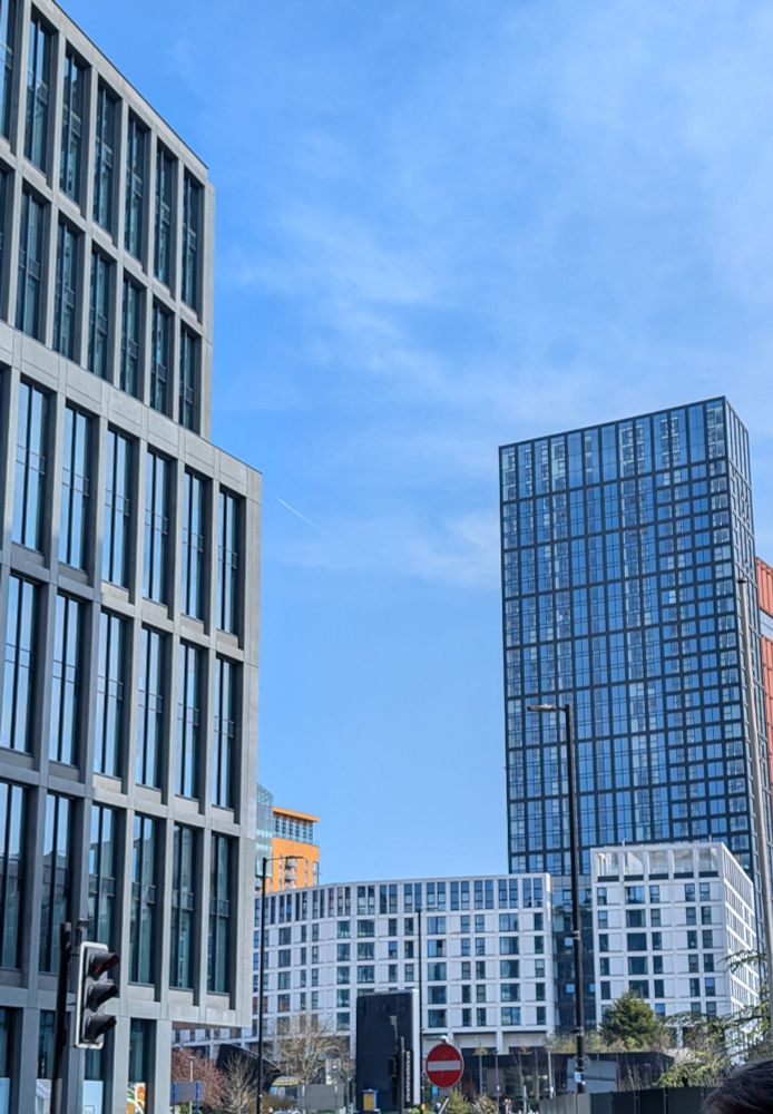 Centre of Manchester, skyscraper in the foreground and background. In the middle is a modern white building, built on the site of Arkwright's first cotton mill