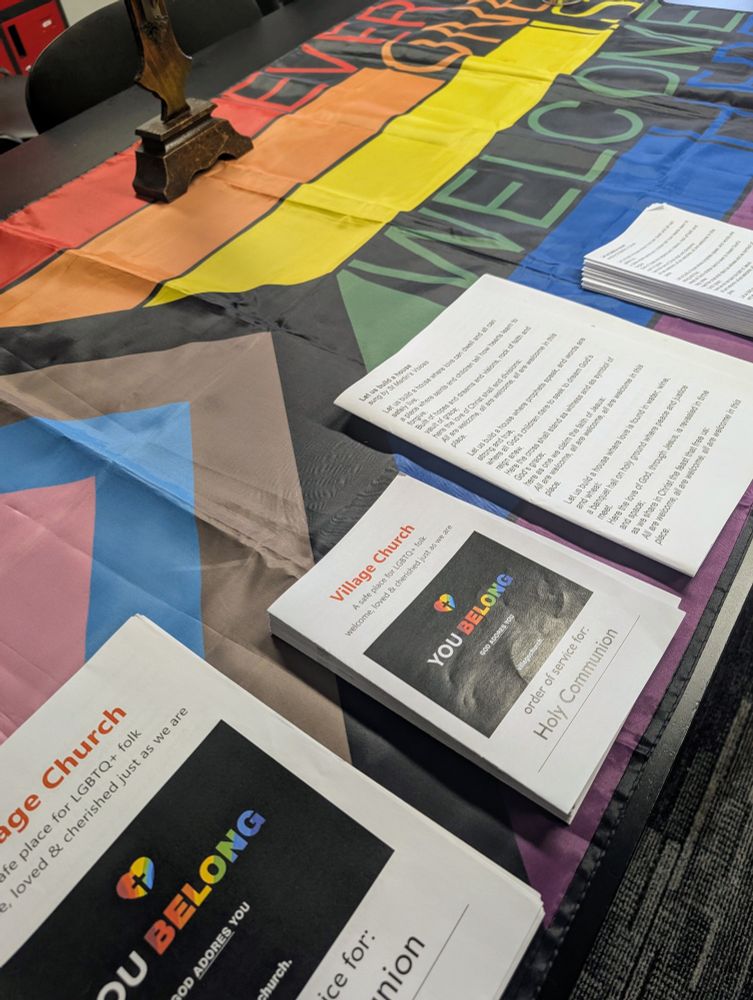 Table at the entrance of the Village church. Orders of service on top of a large progress flag