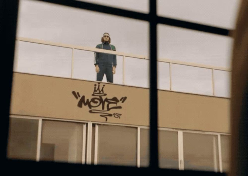 a man standing on top of a building with graffiti on the side that says " more "