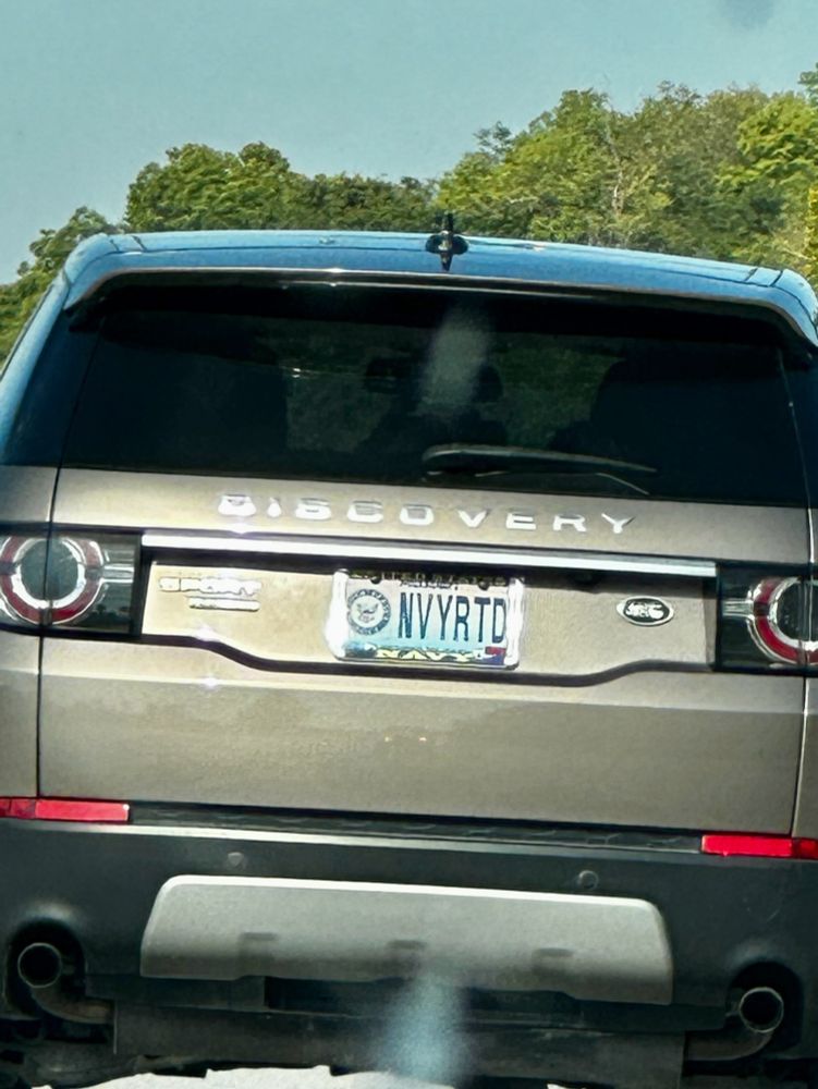 The back of a tan Land Rover Discovery with a custom license plate “NVYRTD” and accompanying Navy license plate frame