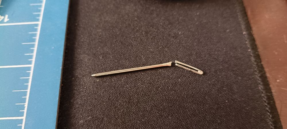 mesa com deskpad preto, base de corte azul e uma agulha quebrada