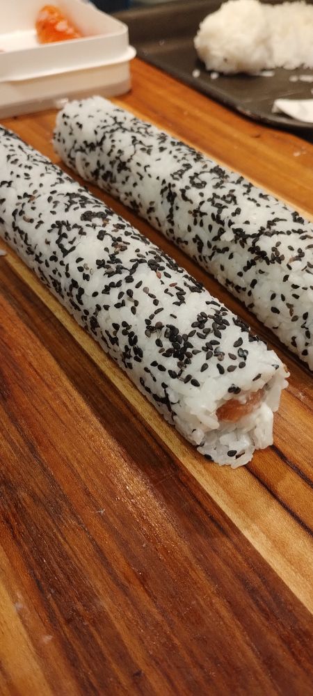 rolos de hosomaki de salmão e  cream cheese prontos pra serem cortados sobre uma base de corte em madeira