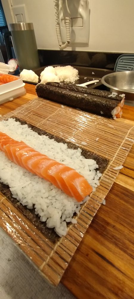 rolos de sushi uramaki de salmão sendo preparados pra cortar sobre base de corte em madeira