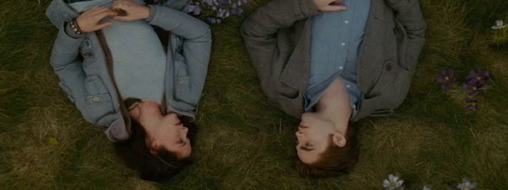 a man and a woman laying in the grass with their heads together