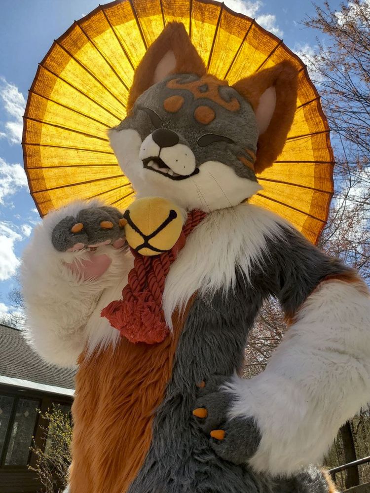 A kemono fox fursuiter holding a parasol with light from the sun shining directly behind it