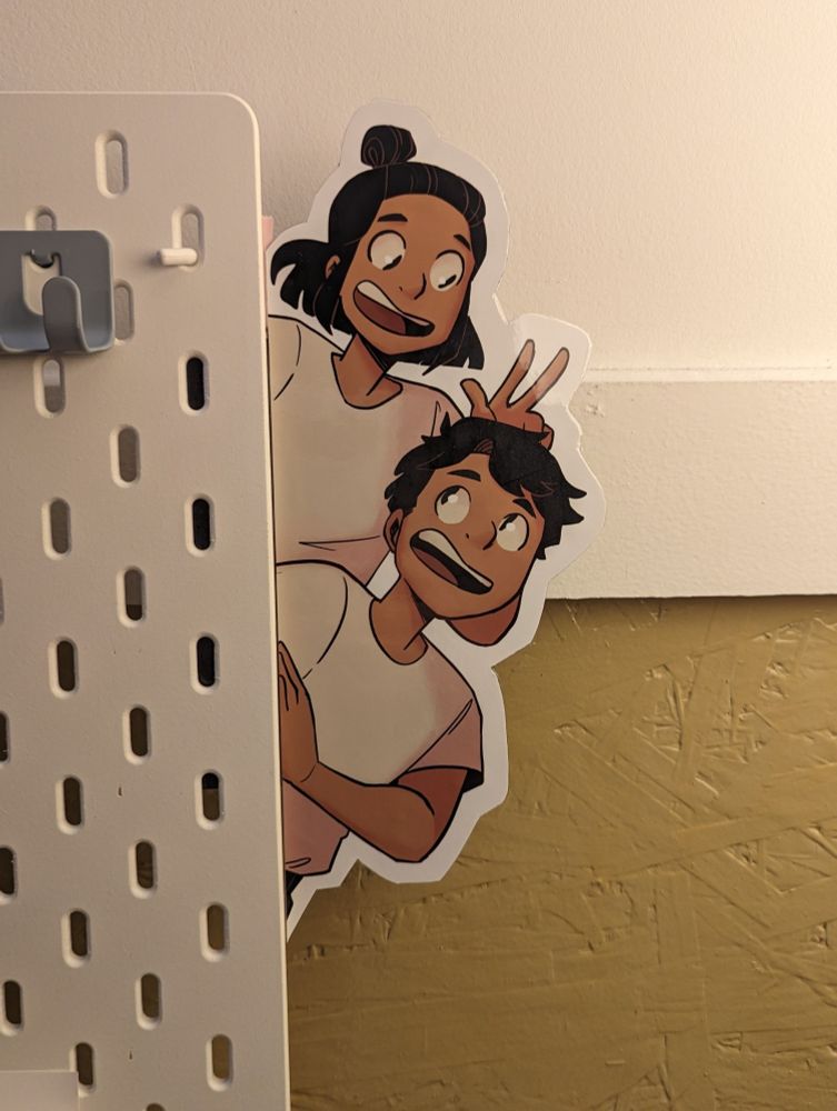 Liza and Elliot cut out from the secret of the ravens peeking out behind a pegboard.