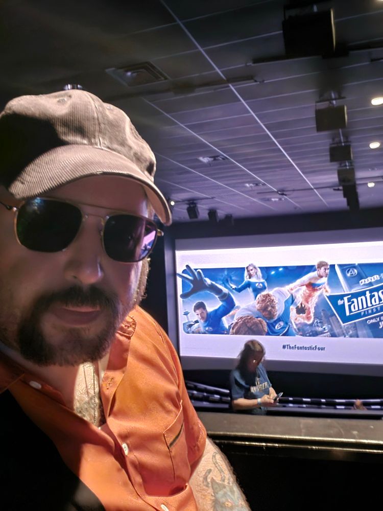 Bearded fellow in a movie theater... behind him and ad for The Fantastic Four: First Steps and the movie's July 25th release date.