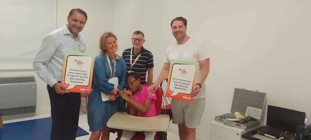 Optometrist Lisa, Dispensing optician Martin and MP Shockat with a child at our special schools eye care service, holding signs promoting eye care rights for those with learning disabilities.