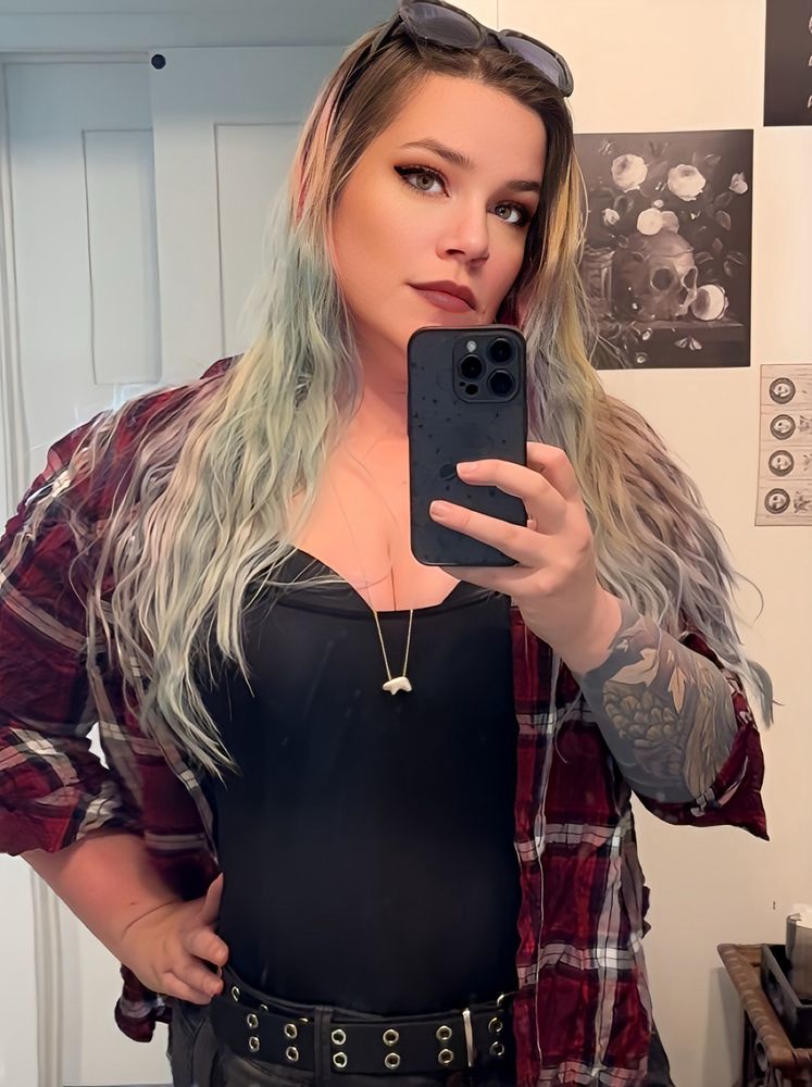 A caucasian woman with a red flannel over a black top, she had multicolored hair, dark eyes, and visible tattoos
