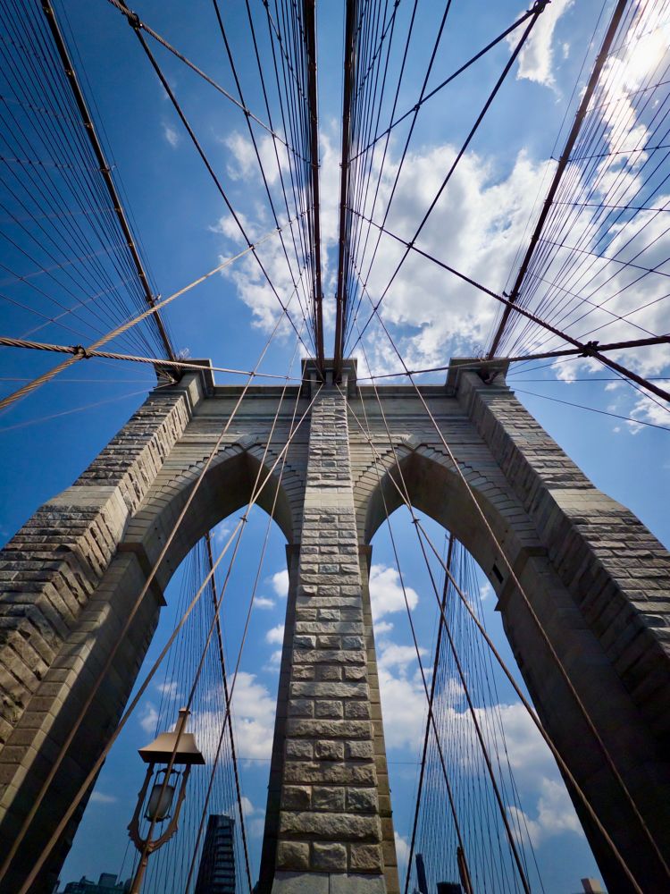 Image of a span of the Brooklyn Bridge with a slightly-cloudy sky in the background.