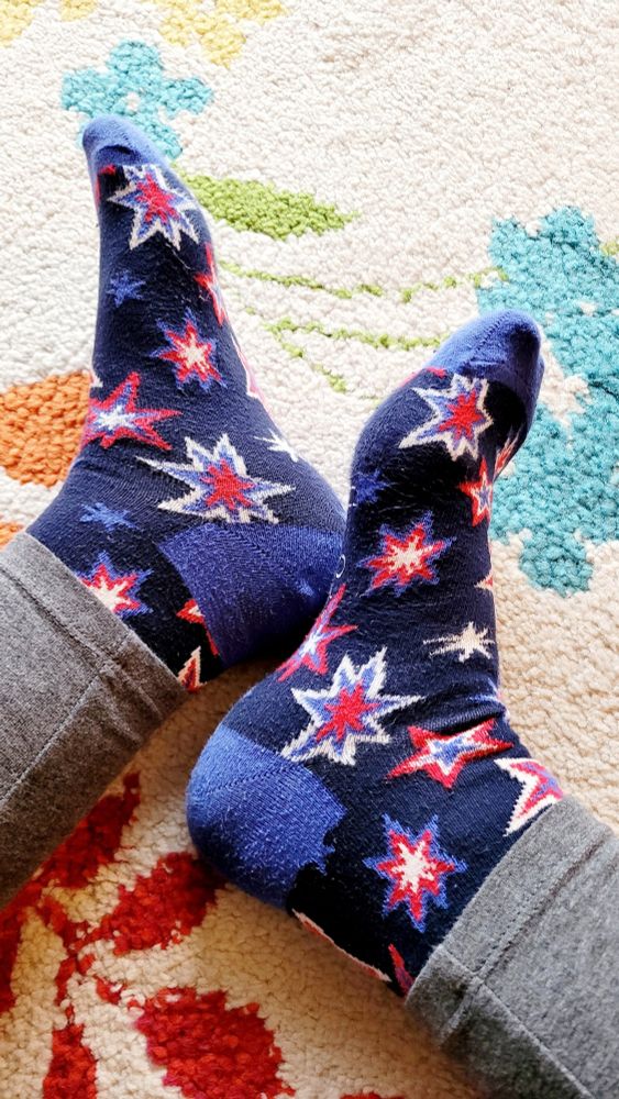 Füße, die in Feuerwerksocken stecken, auf einem bunten Teppich.