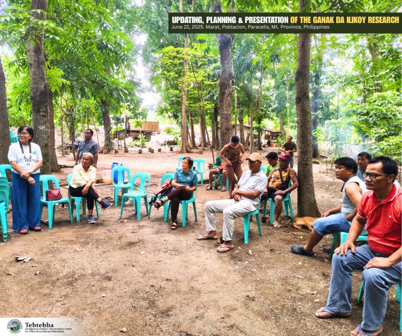 A group of people of Filipino descent sit around in a semi circle outside listening to a presentation