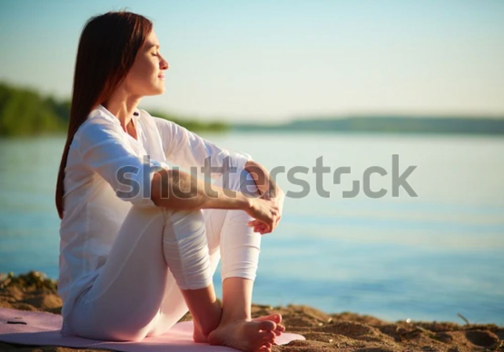 a peaceful looking woman sitting by a lake with her eyes closed