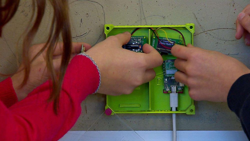 Zwei Handpaare setzen elektronische Bauteile in ein grünes Gehäuse.