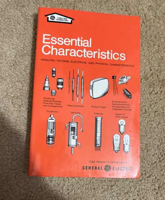 A book with an orange cover. It is called Essential Characteristics. It has black and white illustrations of various electronics related items like picture tubes. At the bottom it shows it was put out by General Electrics.