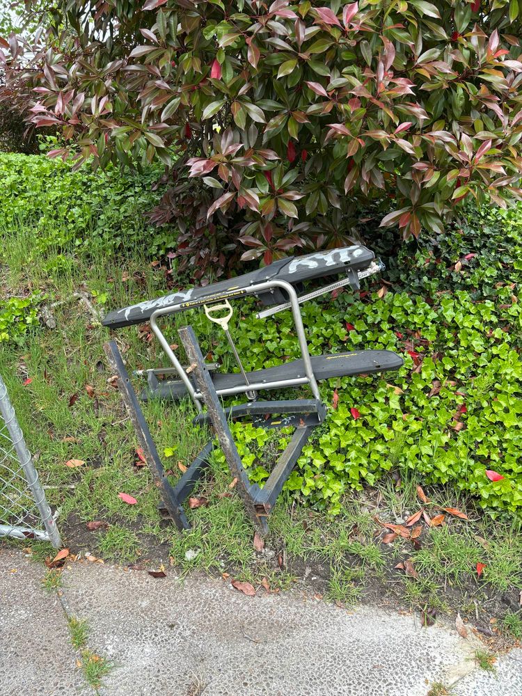 Bike rack assembly that’s been pulled from the ground, covered in graffiti, and is laying in some bushes. 