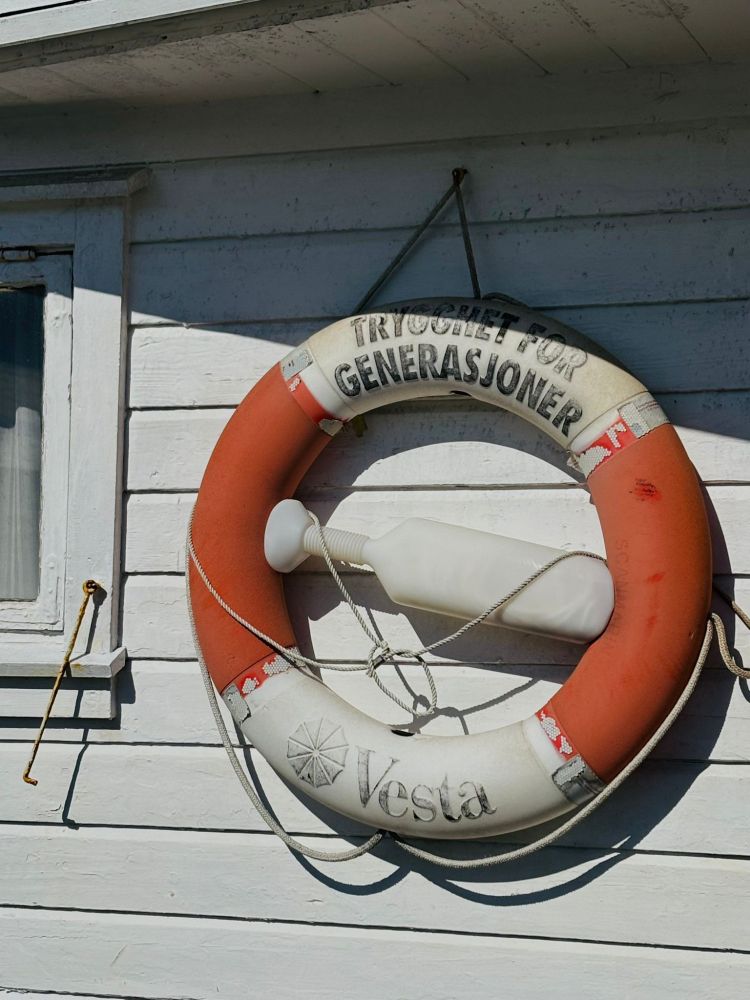 Ein Rettungsring, der an der Wand einer Bootshütte hängt, die weiß angestrichen ist. 
📸 in Norwegen 