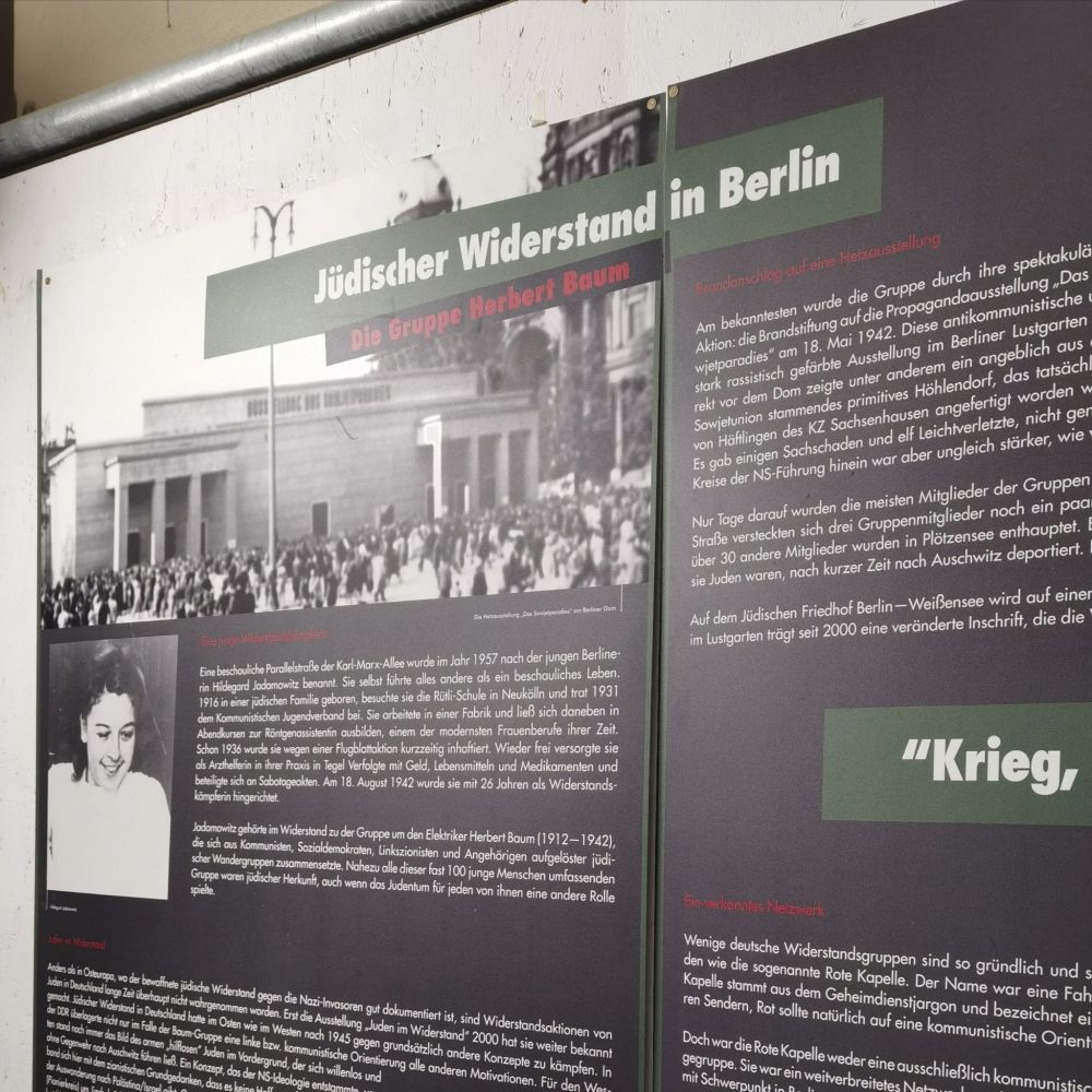 Das Foto zeigt die Exponattafel, mit der im "Jugend[widerstands]museum" in Berlin-Friedrichshain u. a. an Hildegard Jadamowitz erinnert wird, eine junge, kommunistische Widerstandskämpferin gegen das NS-Regime. Der Schriftzug "Jüdischer Widerstand" in Berlin befindet sich in weißer Schrift auf grünem Grund im Kopfbereich der Tafel. Die Tafel weist zudem ein schwarz-weißes Portraitfoto von Hildegard Jadamowitz und ein weiteres Foto aus der NS-Zeit auf, zudem finden sich biographische Begleittexte in weißer Schrift auf schwarzem Grund.