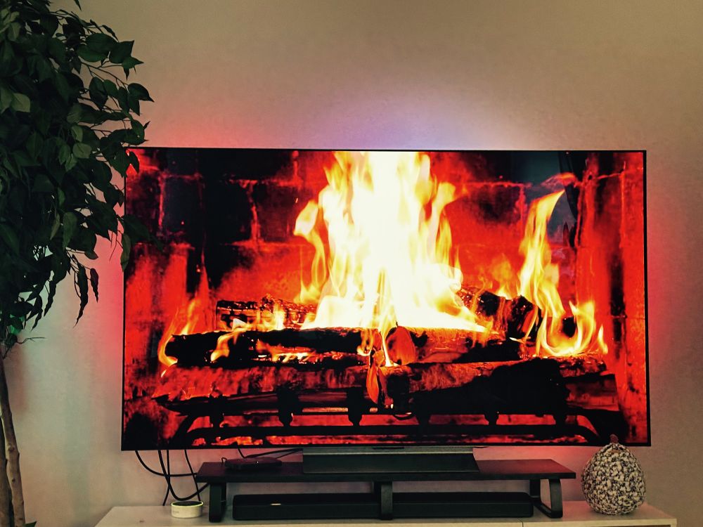 A video of birch logs burning in a fireplace playing on a large screen television. It takes up most of the picture. 