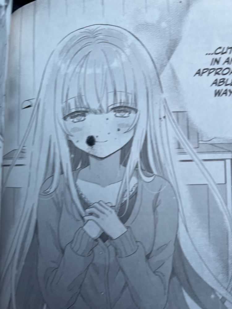 Photo of a page from a manga, with a misprint causing an ink splotch on a girls face.