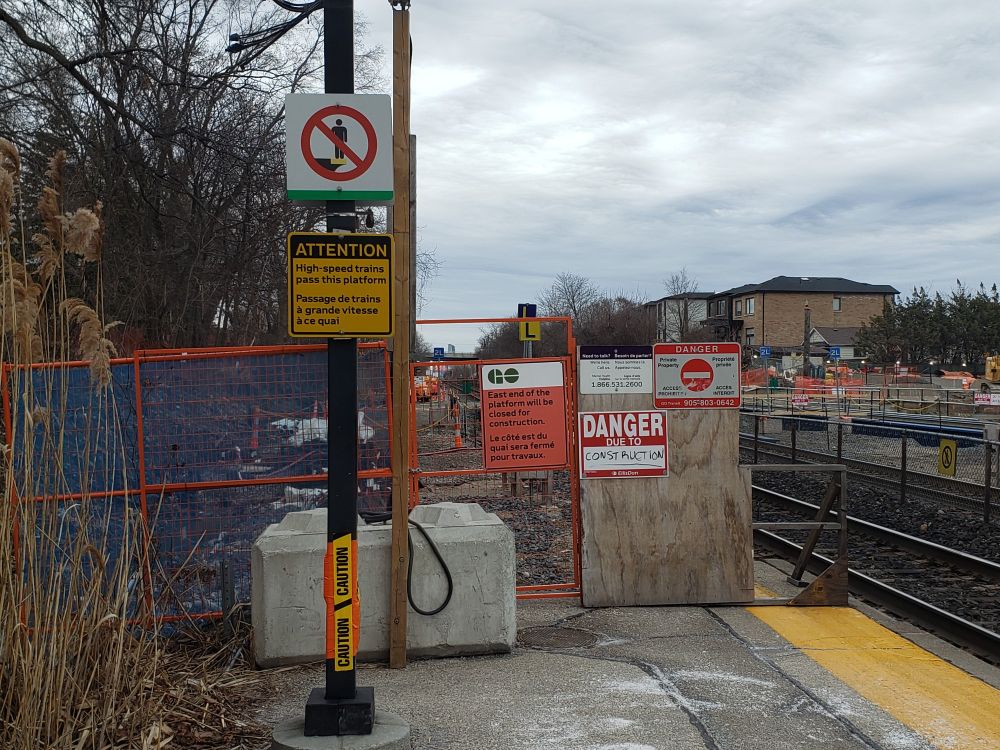 Many signs at a railway station, with train tracks.
