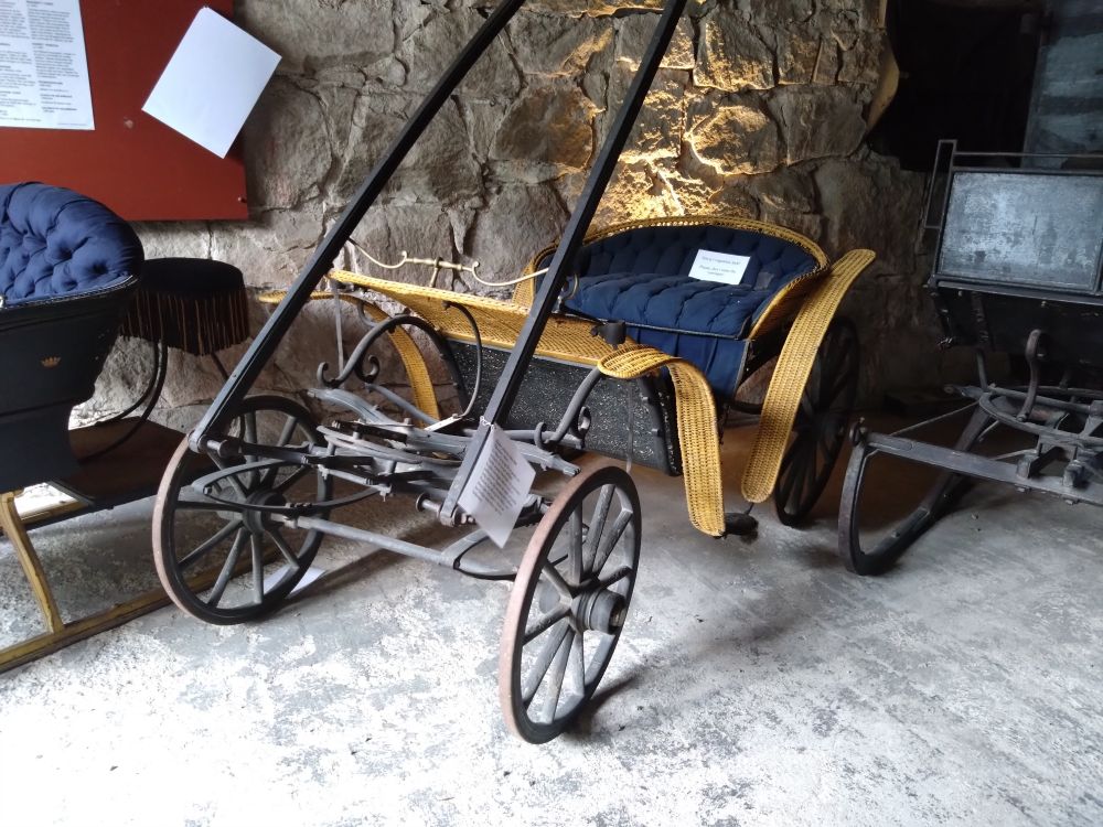 Liten öppen hästvagn med en soffa och flätade skärmar