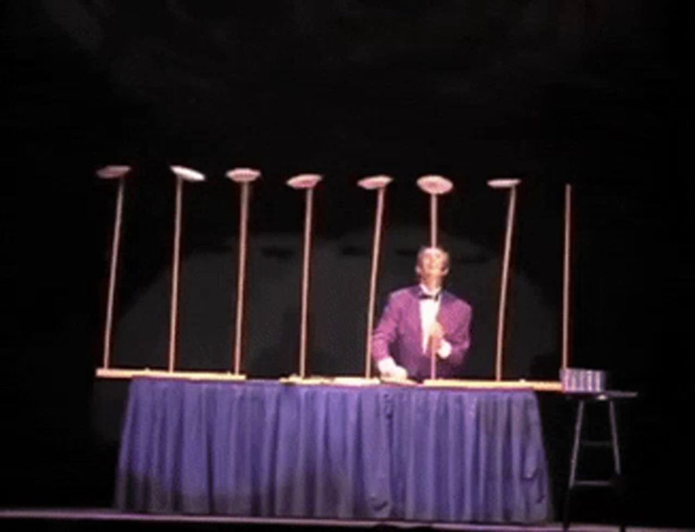 a man in a tuxedo is juggling plates on poles on a stage