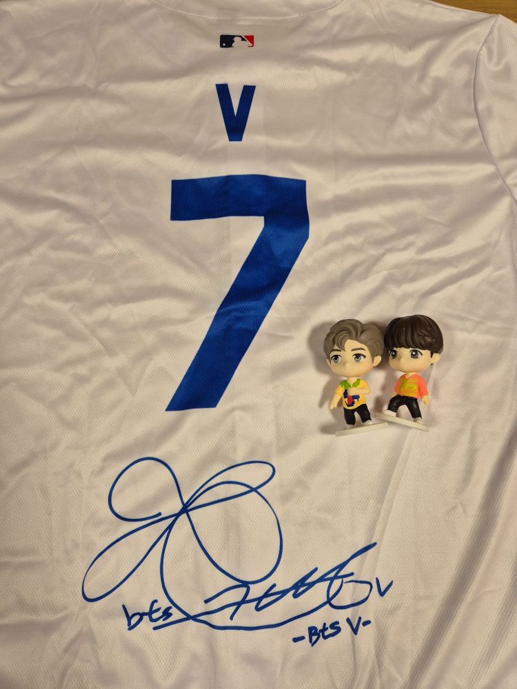 A photo of a replica baseball shirt of the one Kim Taehyung wore at the Dodgers game, and two TinyTan figurines, Namjoon and Yoongi