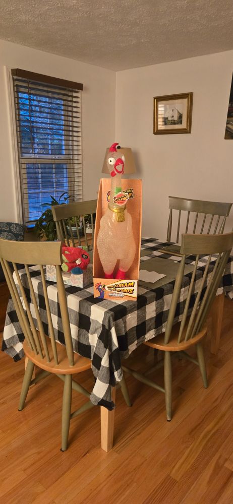 A photo of a large toy chicken on a dining room table. 