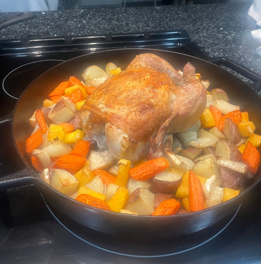A roasted chicken on a bed of root vegetables in a cast iron skillet 