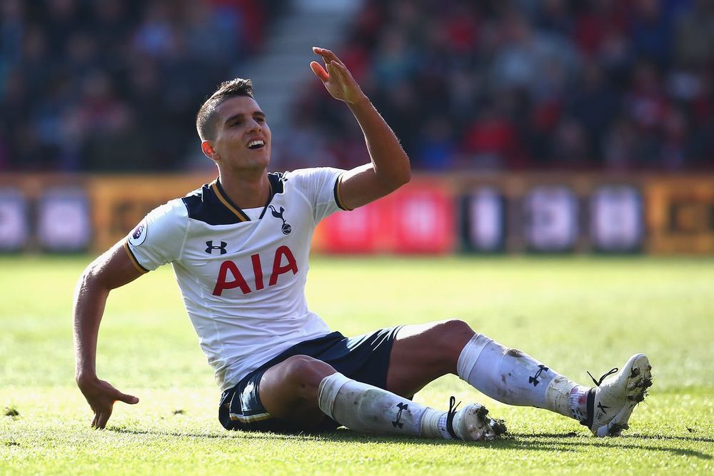 Erik Lamela sitting on a football pitch with his hand in the air.