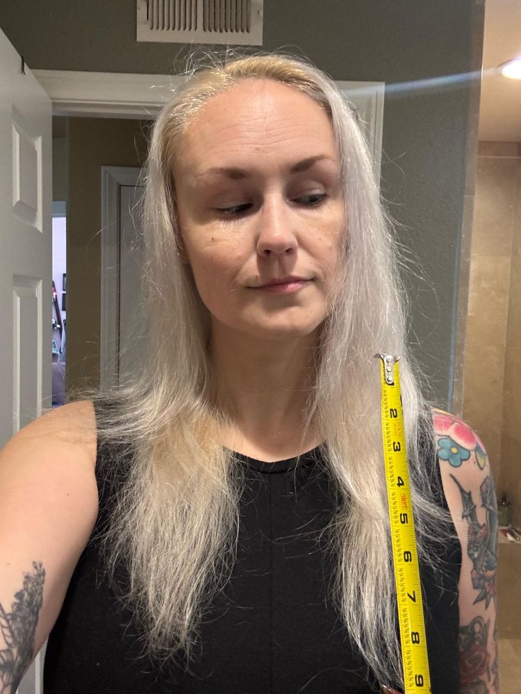 Blonde woman with long hair holding up a measuring tape to her hair 