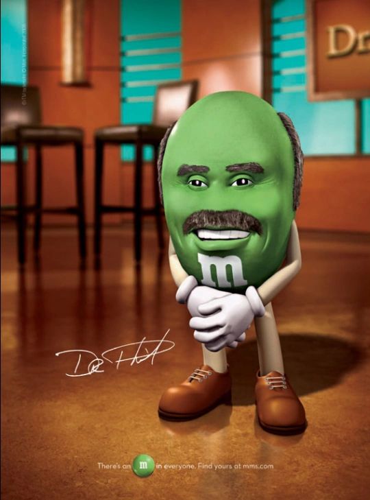 Green Dr. Phil M&M standing in a live television studio with hands crossed around hip height, very stylish shoes and moustache